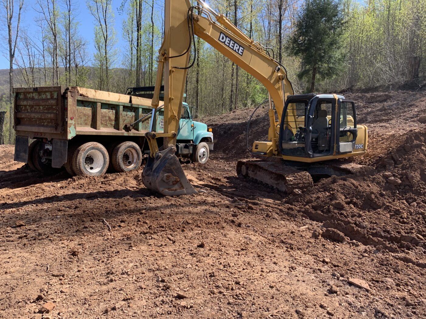 the beginning work of site preparation for a prefab log cabin with a bulldozer and dump truck