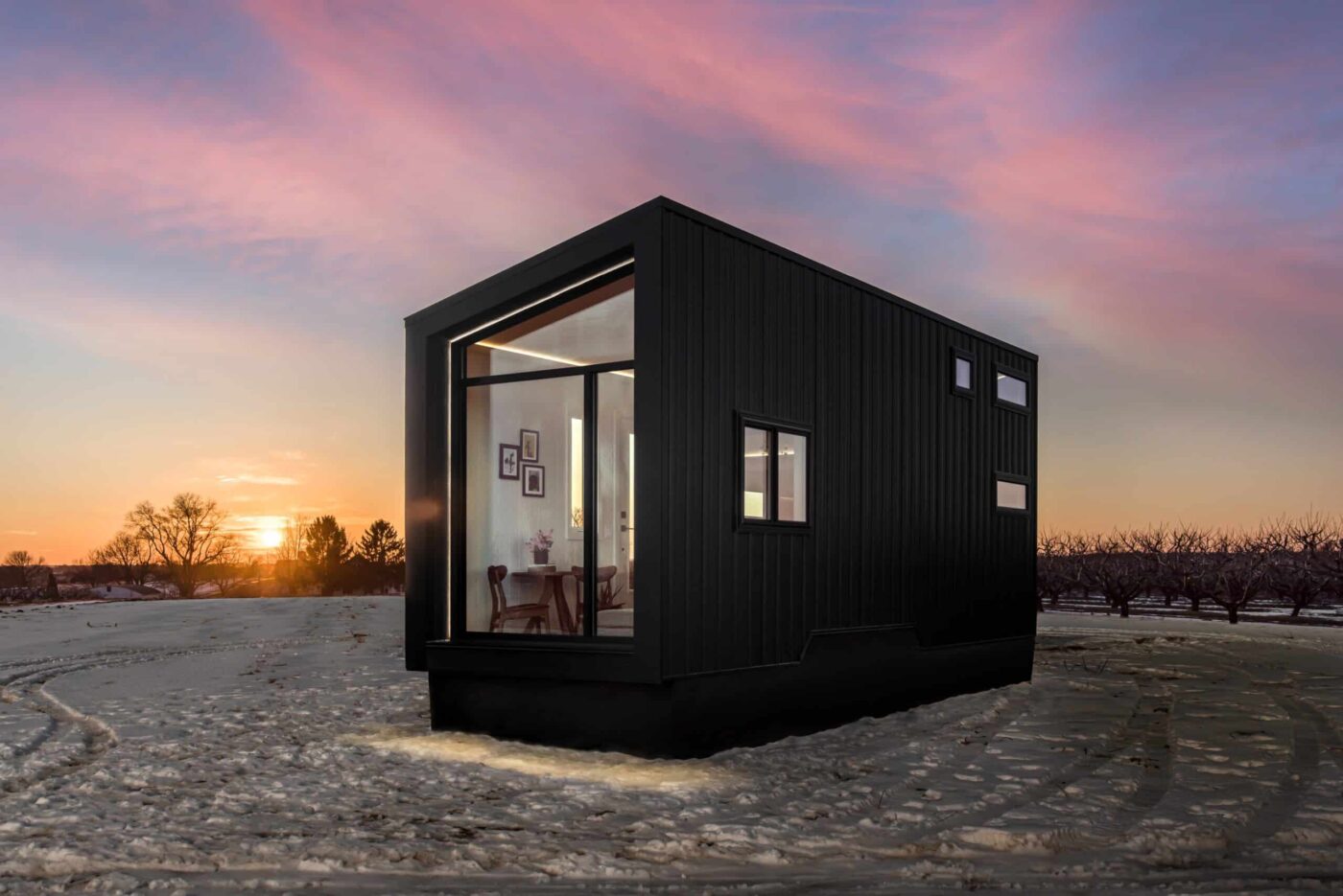 Exterior of Luna Park Model tiny home with modern black siding and large glass windows at sunset.
