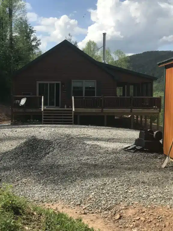 View of dark stained log cabin in garden with iron fence, steps, and porch