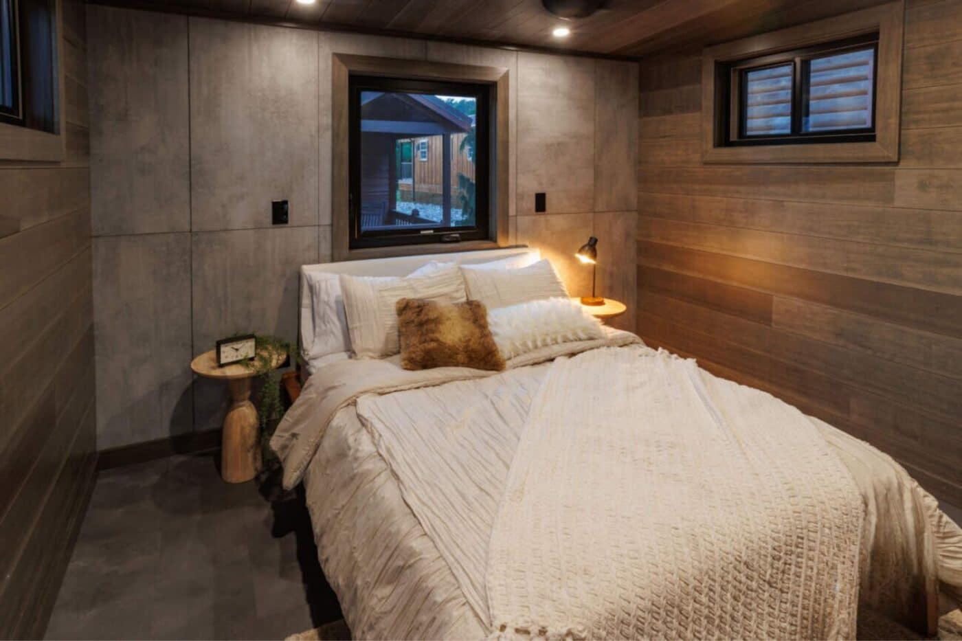 Inside bedroom of Tennessee tiny home with white bed and bedside tables. Windows show neighboring tiny homes