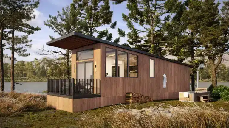 Cozy wooden tiny home with large windows, nestled beside a peaceful lake and surrounded by tall pine trees, with a stack of firewood and a hot tub nearby.