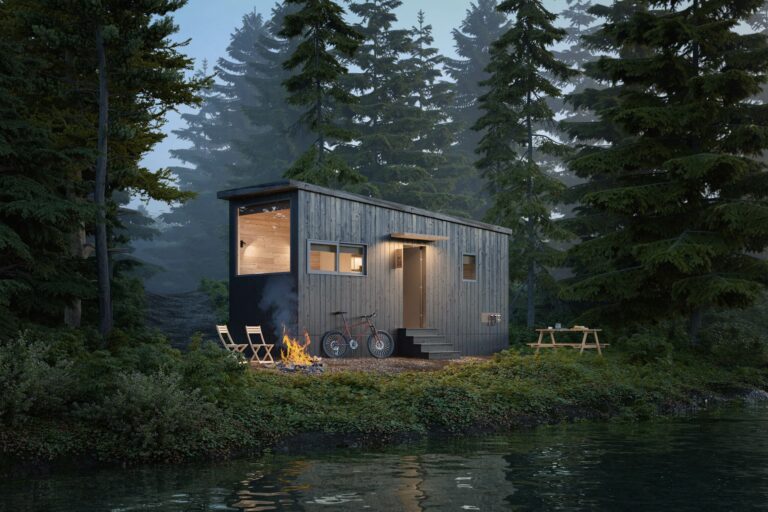 A modern tiny home with dark wood siding is nestled in a lush forest by the edge of a calm lake. The home features large windows that reveal a warmly lit wooden interior. Outside, a campfire burns brightly, surrounded by folding chairs and a parked bicycle. A picnic table is visible to the side, blending into the serene natural setting of tall evergreen trees and dense foliage.