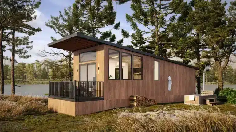 Modern tiny home with a slanted roof, large windows, and a wooden exterior situated in a serene forest setting by a lake. The home features a cozy deck with black railings and a stack of firewood nearby, complemented by a hot tub and seating area surrounded by tall trees and natural grass.