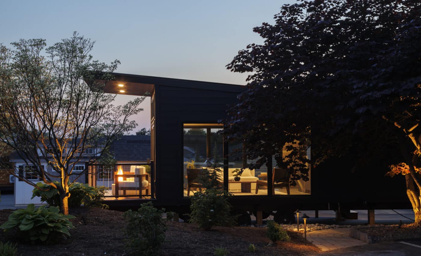 side view of park model tiny home with lights on at night surrounded by trees